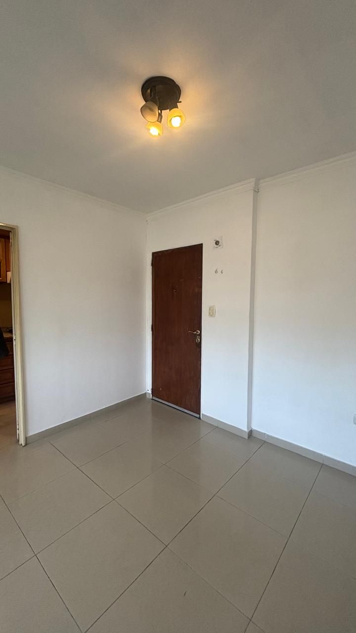 Ambiente vacío con puerta de madera al fondo y piso cerámico
